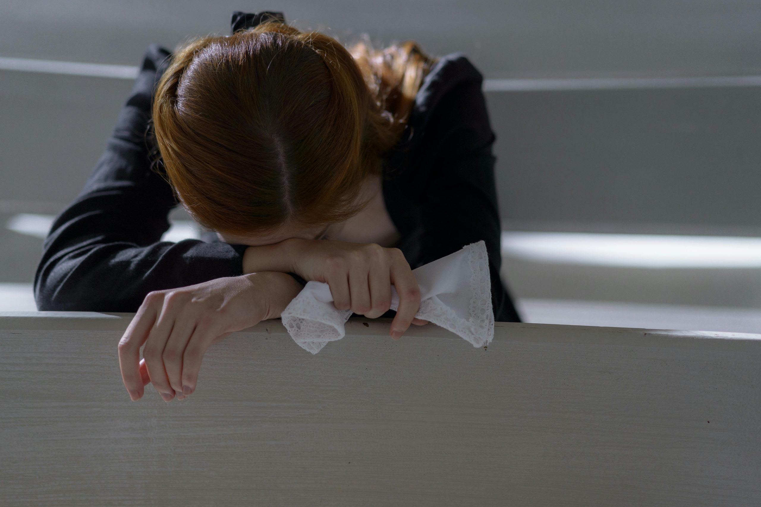 A woman leans on a bench in a peaceful church, lost in thought and prayer.